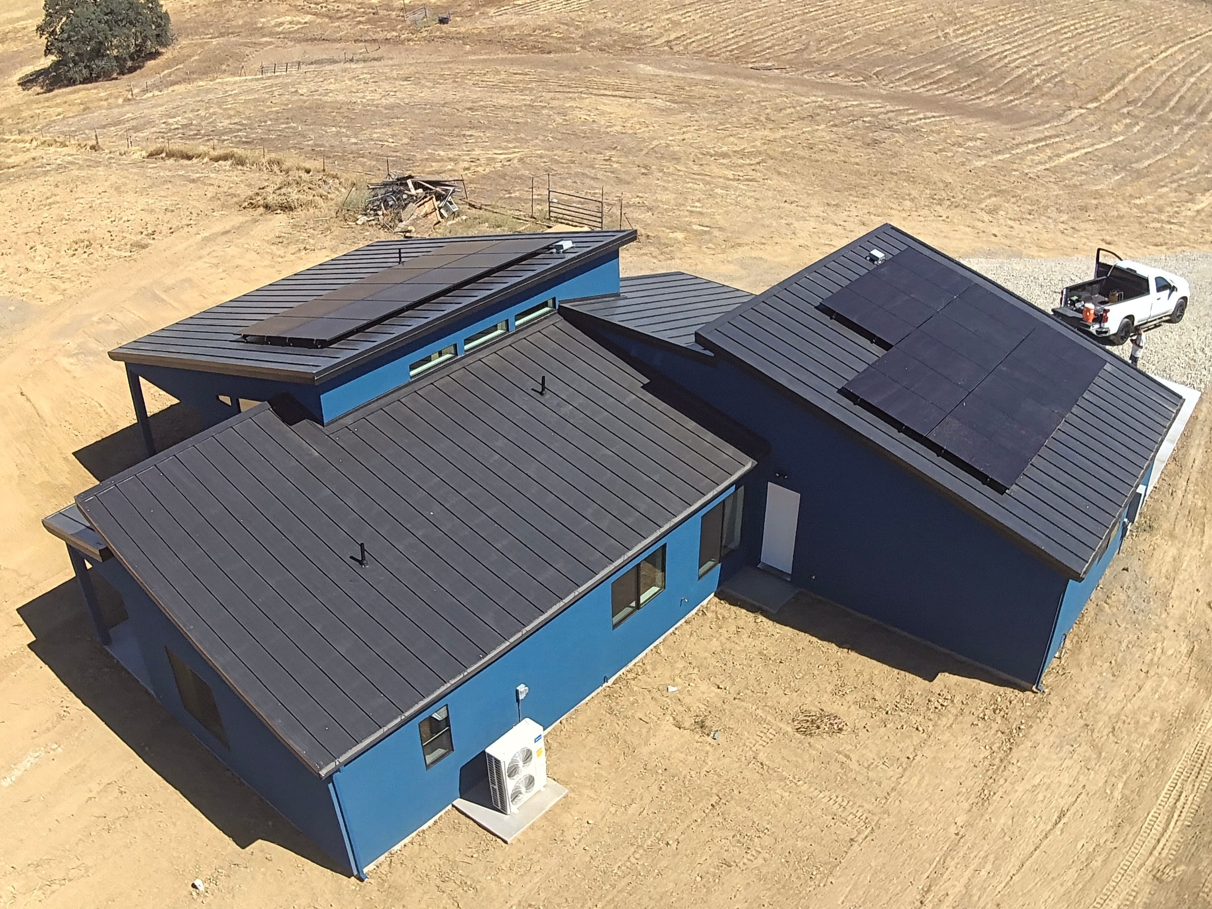 Aerial view of a finished standing-seam metal roof with solar panels on a rural home