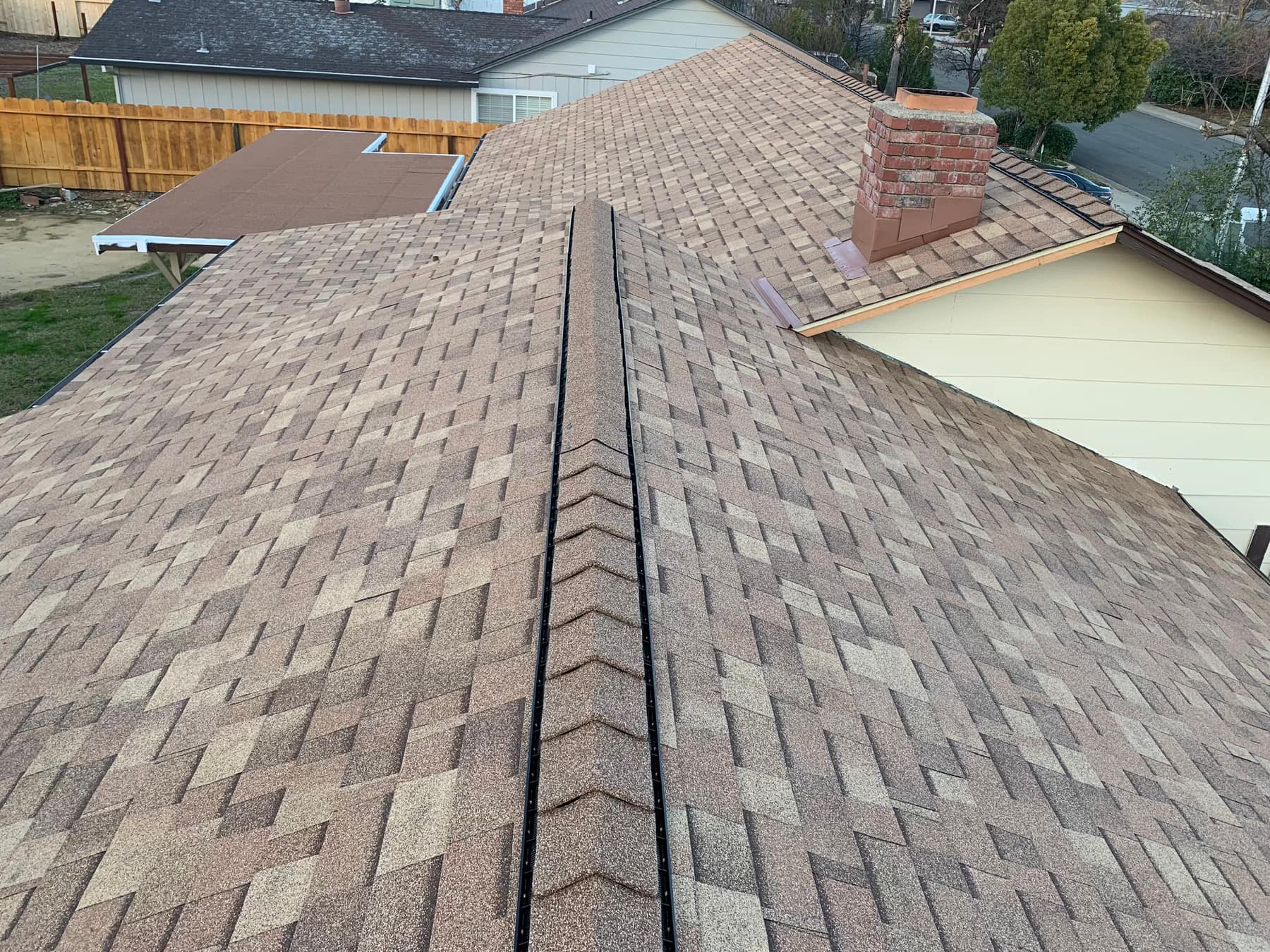 Aerial view of a completed composite shingle roof with a brick chimney