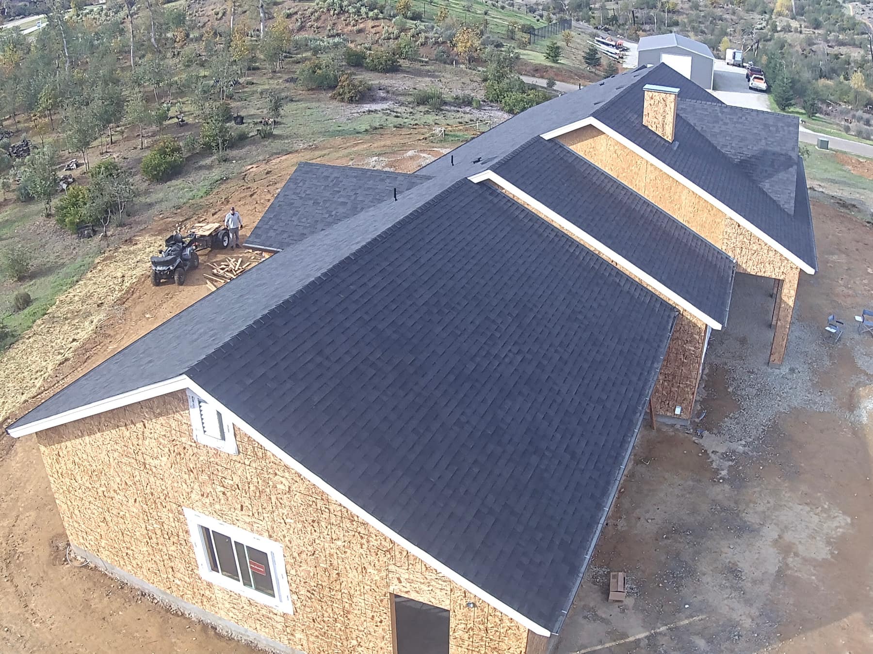 Aerial view of a large custom home mid-construction with a new shingle roof