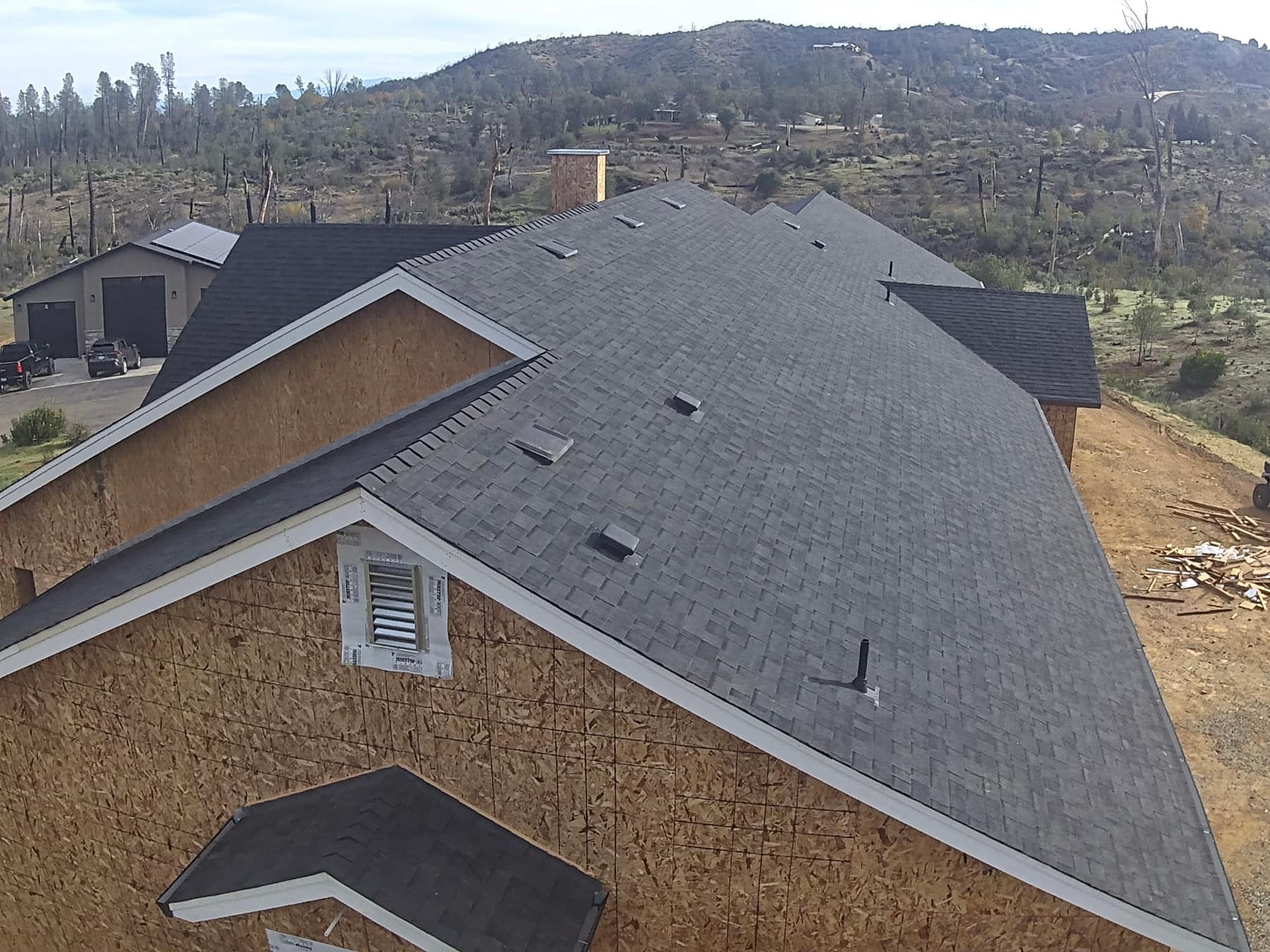 Aerial view of a large custom home with a new shingle roof on a hillside property