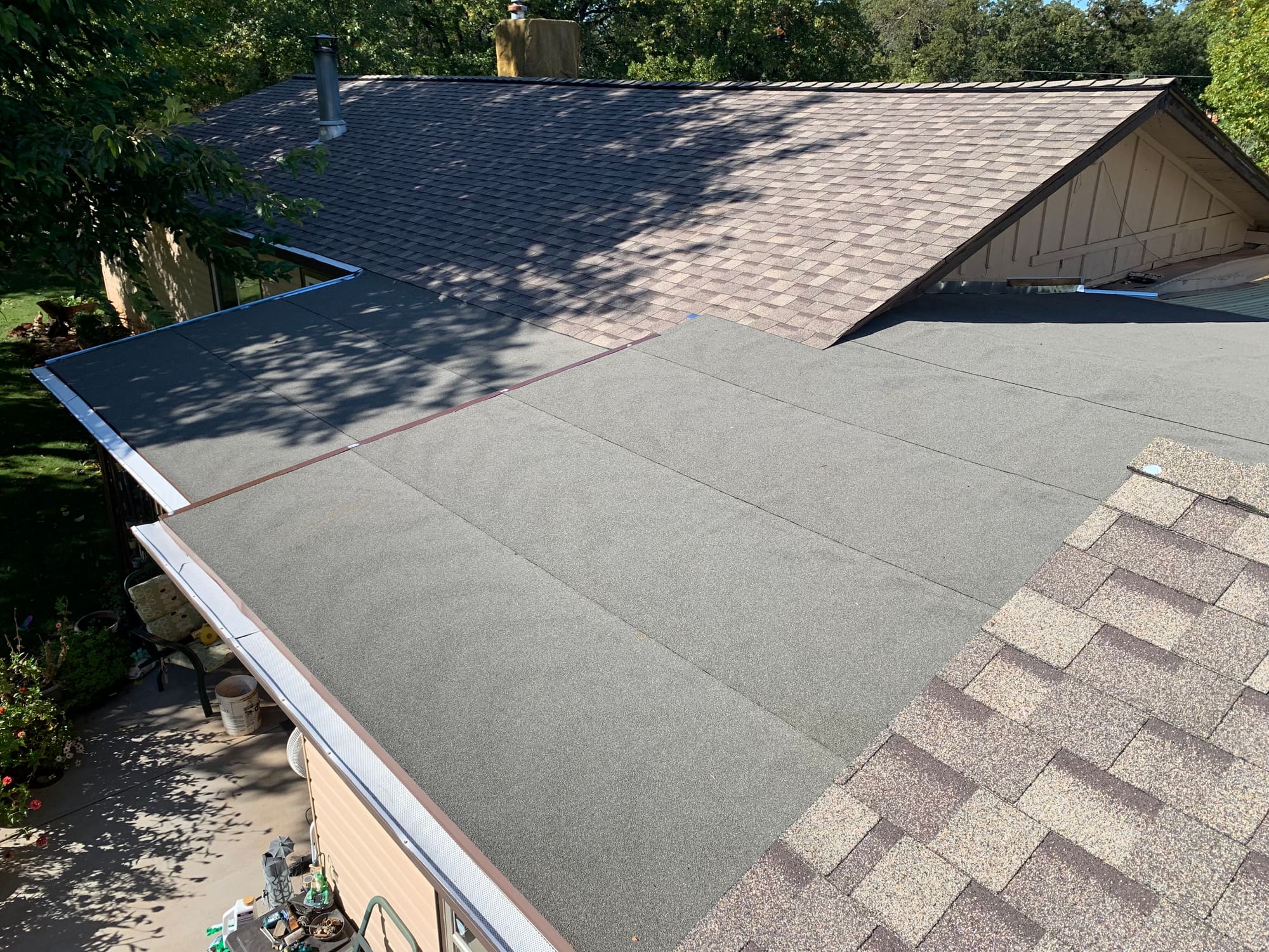 Finished low-slope roof section with a self-adhered cap sheet, transitioning to an asphalt shingle roof