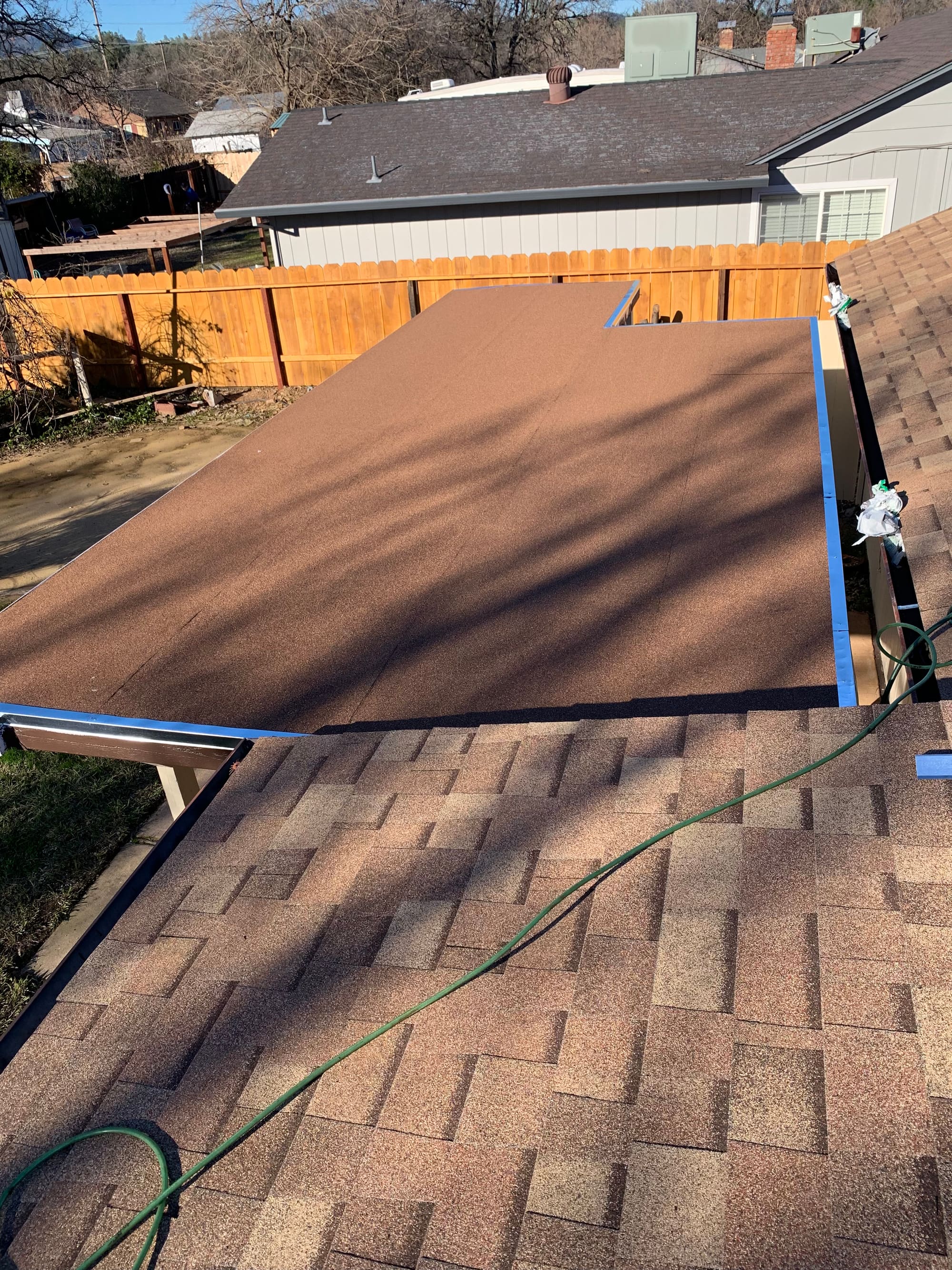 Finished low-slope roof section on a porch, next to an asphalt shingle roof